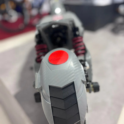 Izdelek na sliki je električni skiro, model Eco Speed 10X V2. Na sliki je vidna zadnja stran skiroja, kjer so prikazani amortizerji v rdeči barvi ter del zadnjega kolesa s profilom pnevmatike. Vidna je tudi odsevna oznaka v rdeči barvi, kar povečuje varnost pri vožnji. Skupna zasnova skiroja je moderna in funkcionalna.