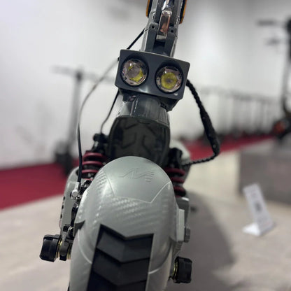 Izdelek na sliki je električni skiro, model Eco Speed 10X V2. Na sliki je vidna sprednja stran skiroja, ki ima dva svetlobna elementa, kar nakazuje na možnost osvetlitve. Vidni so tudi amortizerji in detajli na kolesu, kar nakazuje na robustno konstrukcijo in namenjenost za udobno vožnjo.