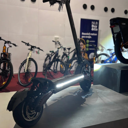 Na sliki je električni skiro, model Eco Speed 10X V2. Izdelek ima moderno zasnovo in je opremljen s svetlobnimi elementi, ki povečujejo vidnost. V ozadju so vidni tudi drugi kolesi, kar nakazuje, da je skiro del razstave ali trgovine s kolesi.