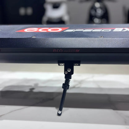 Izdelek na sliki je električni skiro, model Eco Speed 9X. Na sliki je vidna površina skiroja z logotipom "eco" in "speed 9X", ter del mehanizma, ki je verjetno povezan s sistemom za zlaganje ali stabilizacijo. Ozadje je zamegljeno, kar nakazuje, da je izdelek postavljen v trgovinskem okolju.