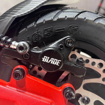 Na sliki je del električnega skiroja, model "Eco Speed 9X". Vidna je zadnja kolesna enota, ki vključuje zavorni sistem in pnevmatiko. Zavorni sistem je označen z znamko "Blade", kar nakazuje na kakovostno izvedbo. Pnevmatika je širša, kar omogoča boljšo stabilnost in oprijem pri vožnji. Rdeča barva delov dodaja estetski element celotnemu dizajnu.