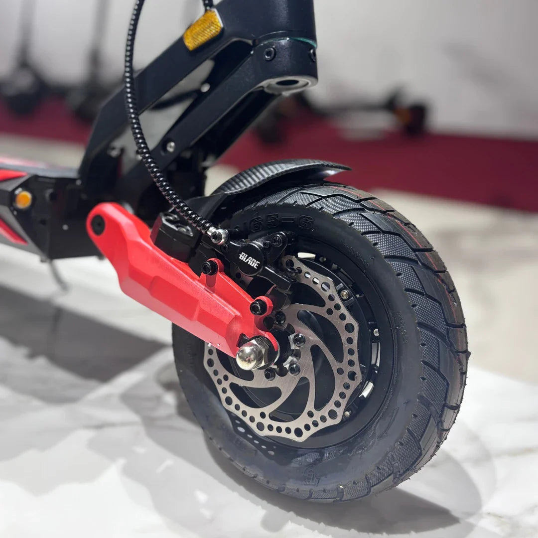 Izdelek na sliki je električni skiro, model Eco Speed 9X. Vidna je zadnja kolesa z disk zavornim sistemom in robustnim gumami, kar nakazuje na dobro oprijemljivost in stabilnost. Rdeči del, ki je del zavorne mehanizacije, izstopa in dodaja športen videz. Skuter je zasnovan za urbano vožnjo, kar je razvidno iz njegove kompaktnosti in funkcionalnosti.