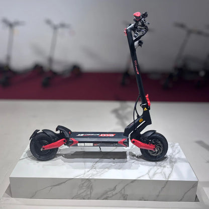 Izdelek na sliki je električni skiro, model Eco Speed 9X. Na sliki je prikazan skiro, ki ima črno in rdečo barvno kombinacijo, široka kolesa in robustno konstrukcijo. Vidna je tudi krmilo z različnimi kontrolami, kar nakazuje na funkcionalnost in udobje pri vožnji. Skuter je postavljen na elegantno podlago, kar poudarja njegov dizajn. V ozadju so vidni še drugi skiroji, kar nakazuje na razstavo ali prodajno mesto.