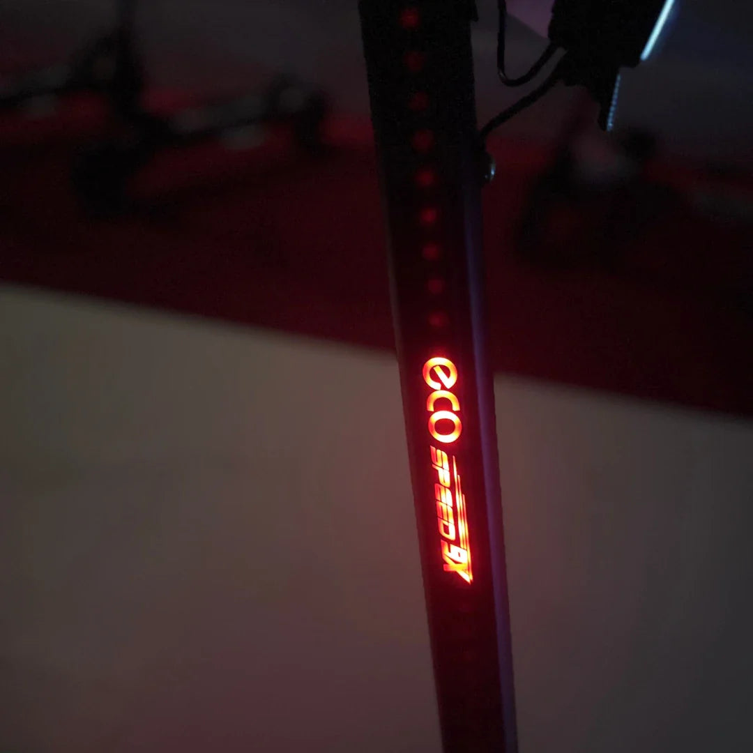 Izdelek na sliki je električni skiro, model Eco Speed 9X. Na sliki je vidna osvetlitev na telesu skiroja, kjer je jasno izpisano ime "eco speed". Osvetlitev je rdeča, kar nakazuje na funkcionalnost, ki lahko vključuje varnostne elemente za vožnjo v temi. V ozadju se lahko opazijo tudi drugi skiroji.