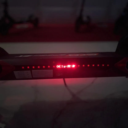 Izdelek na sliki je električni skiro, model Eco Speed 9X. Na sliki je vidna zgornja plošča skiroja, ki ima rdeče LED luči ter oznako znamke. V ozadju so vidni tudi drugi električni skiroji. Plošča vsebuje tudi informacije o delovanju in specifikacijah skiroja.