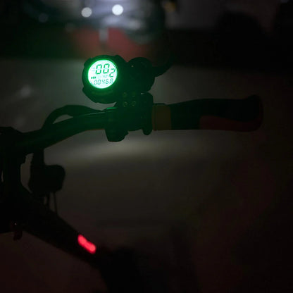 Na sliki je električni skiro, model Eco Speed 9X. Vidna je ročica s prikazovalnikom, ki kaže hitrost in druge podatke, obarvana v zeleno. V ozadju je slabo osvetljen prostor, kar nakazuje, da je slika posneta v temi. Ročaj skiroja je opremljen z barvnimi detajli, kar prispeva k njegovemu modernemu videzu.