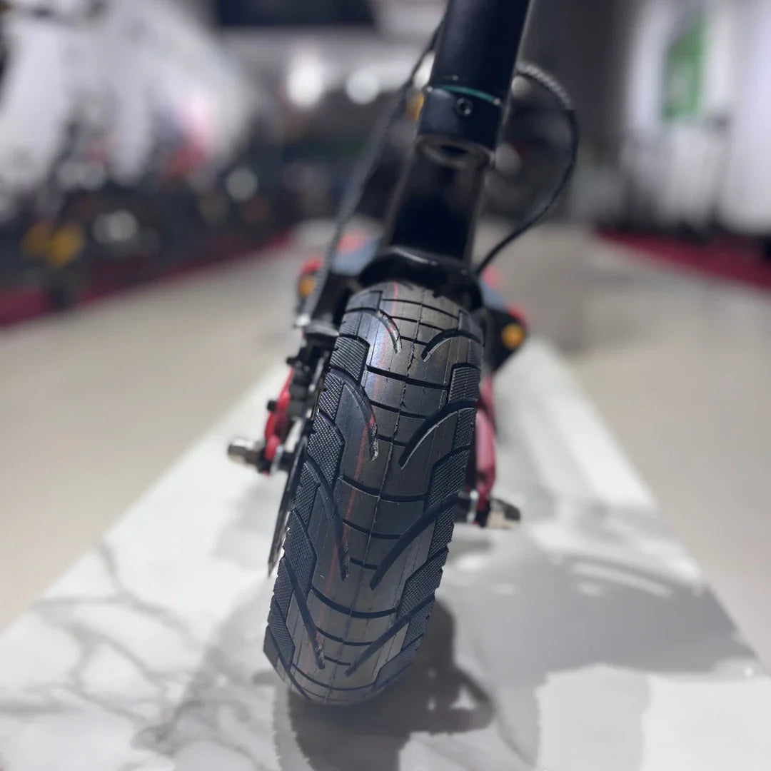 Izdelek je električni skiro, model Eco Speed 9X. Na sliki je prikazan zadnji del skiroja, kjer je vidna široka pnevmatika s profilom, ki je zasnovan za dobro oprijemljivost. V ozadju se vidi del prodajnega prostora z drugimi skiroji.