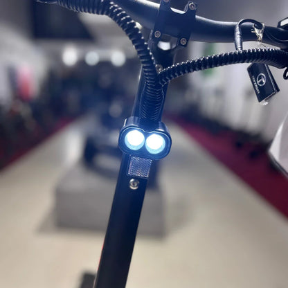 Izdelek na sliki je električni skiro, model Eco Speed 9X. Na sliki je vidna sprednja stran skiroja, kjer so nameščena dva svetila, ki zagotavljata osvetlitev med vožnjo. Skira ima črno barvo in robustno konstrukcijo, kar nakazuje na njegovo vzdržljivost. V ozadju je mogoče opaziti še druge skiroje, kar nakazuje, da je slika posneta v trgovini ali na razstavi.