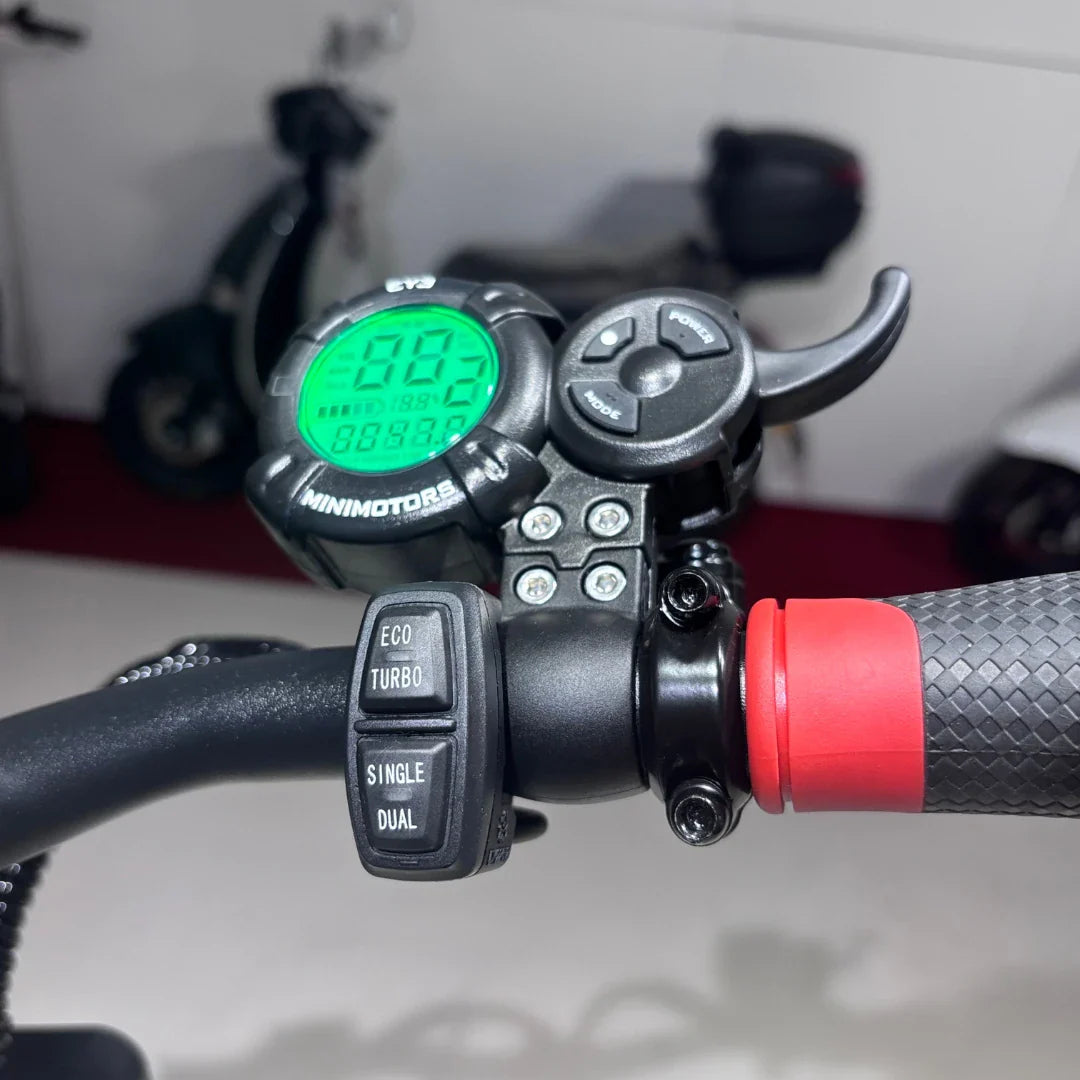 Na sliki je električni skiro, model Eco Speed 9X, znamke Minimotors. Vidni so upravljalni elementi na krmilu, vključno z digitalnim zaslonom, ki prikazuje hitrost in druge podatke, ter gumbi za izbiro načina vožnje (Eco, Turbo, Single, Dual). Rdeč gumijast del na ročaju dodaja udobje pri vožnji.