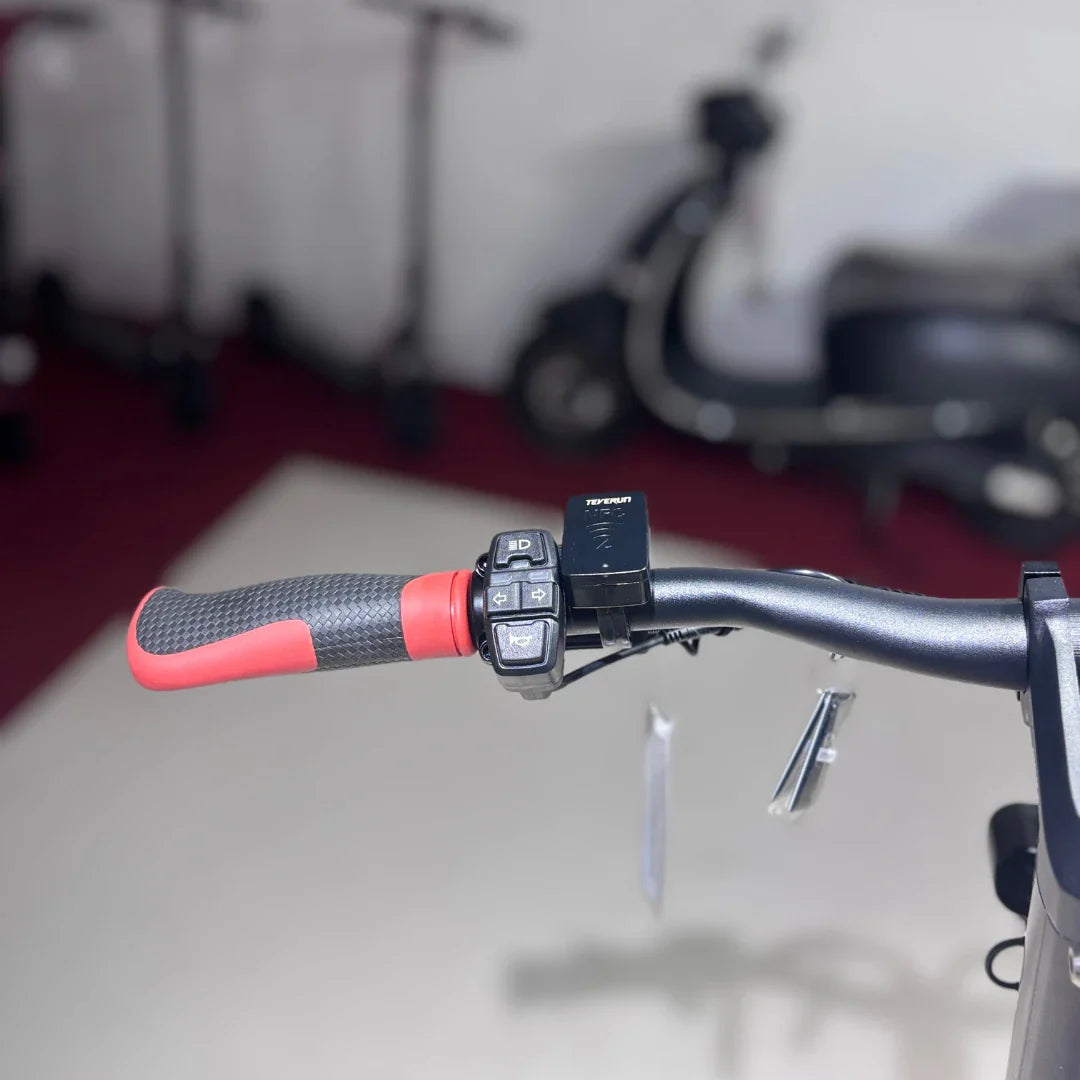 Na sliki je električni skiro model "Eco Speed 9X". Vidni so ročaji skiroja s teksturirano površino za boljši oprijem, ter nadzorna ploščica z različnimi gumbi, ki omogočajo upravljanje funkcij skiroja. V ozadju so vidni drugi skiroji, kar nakazuje, da gre za okolje, kjer se ti izdelki prodajajo ali uporabljajo.