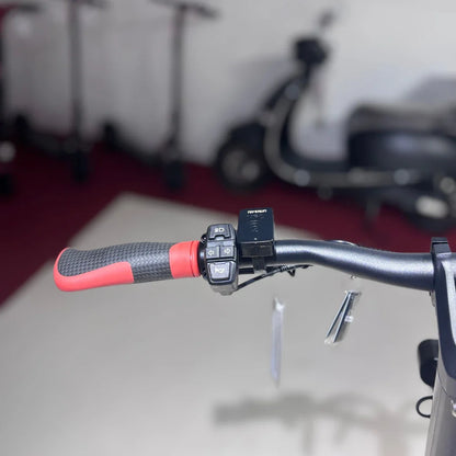 Na sliki je električni skiro model "Eco Speed 9X". Vidni so ročaji skiroja s teksturirano površino za boljši oprijem, ter nadzorna ploščica z različnimi gumbi, ki omogočajo upravljanje funkcij skiroja. V ozadju so vidni drugi skiroji, kar nakazuje, da gre za okolje, kjer se ti izdelki prodajajo ali uporabljajo.