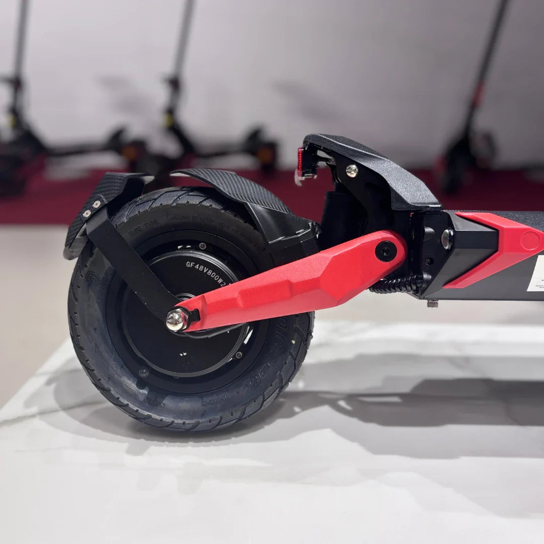 Na sliki je prikazan električni skiro model Eco Speed 9X. Vidna je zadnja kolesna enota, ki vključuje široko pnevmatiko in rdečo podporno ročico. Zasnova skiroja je moderna, s poudarkom na robustnosti in stabilnosti. V ozadju so vidni tudi drugi električni skiroji, kar nakazuje na okolje, kjer se skiroji prodajajo ali razstavljajo.