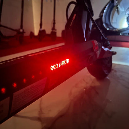 Na sliki je električni skiro model "Eco Speed 9X". Vidna je njegova zadnja stran, kjer se nahaja rdeča LED lučka, ki označuje delovanje skiroja. V ozadju so vidni tudi drugi skiroji, kar nakazuje, da je izdelek del večje zbirke. Skira je zasnovan za urbano mobilnost in udobno vožnjo.