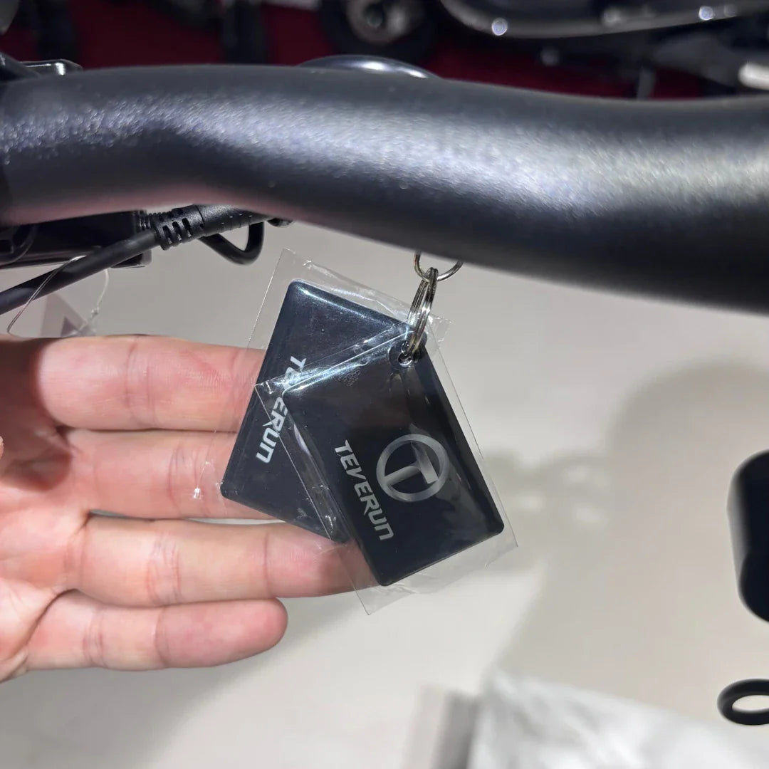 Na sliki je električni skiro, model Eco Speed 9X, znamke Teverun. Vidna je ročica skiroja, na kateri je pripet ključek z logotipom Teverun. Ključek je v prozorni zaščiti, kar nakazuje na novost ali dodatno opremo skiroja.