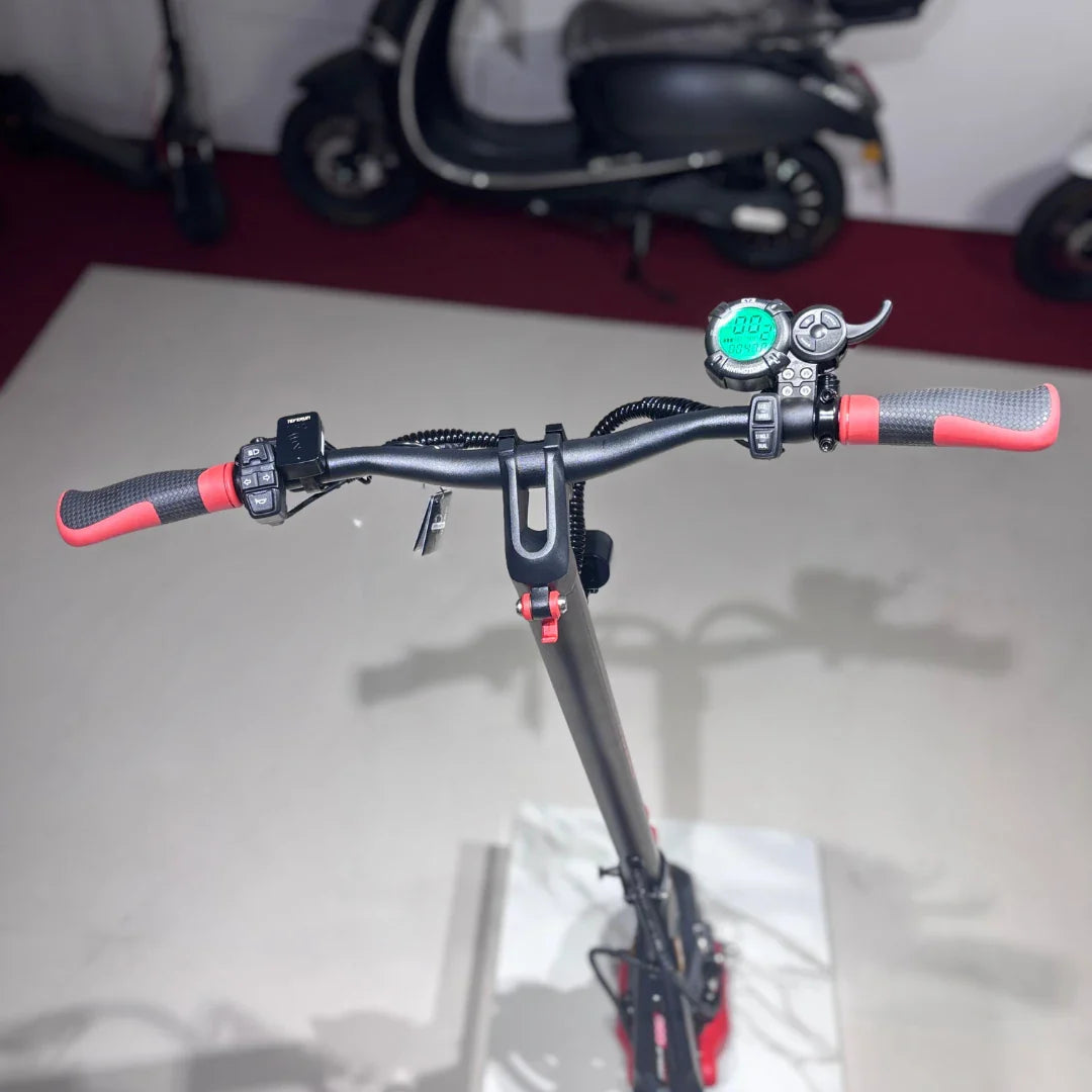 Izdelek je električni skiro, model Eco Speed 9X. Na sliki je prikazan nadzorni del skiroja, kjer so vidni ročaji z rdečimi detajli, digitalni zaslon, ki prikazuje hitrost, ter gumbi za upravljanje. V ozadju so vidni tudi drugi električni skiroji.