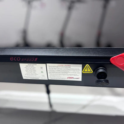 Na sliki je električni skiro z imenom Eco Speed 9. Vidna je oznaka modela na okvirju, skupaj z informacijami o električnem motorju in varnostnimi opozorili. Na skiroju je tudi priključek za polnjenje, kar nakazuje na njegovo električno delovanje. V ozadju so vidni še drugi skiroji, kar daje občutek o širši ponudbi.