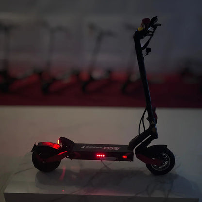 Izdelek na sliki je električni skiro, model Eco Speed 9. Na sliki je skiro postavljen na svetlo podlago, vidna pa je njegova črna in rdeča barvna kombinacija. Ima svetleče LED luči, kar nakazuje na njegovo funkcionalnost tudi v slabših svetlobnih pogojih. V ozadju so vidni še drugi električni skiroji, kar daje občutek o večji izbiri.