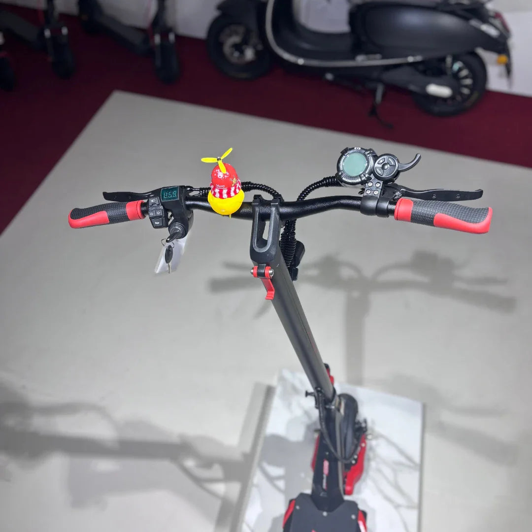 Na sliki je električni skiro, model Eco Speed 9. Vidni so ročaji skiroja, ki imajo rdeče in črne detajle, ter zaslon z informacijami o hitrosti in bateriji. Na ročaju je tudi majhen okras v obliki rdeče in rumene igrače s propelerjem. V ozadju so vidni drugi skiroji in skuterji.