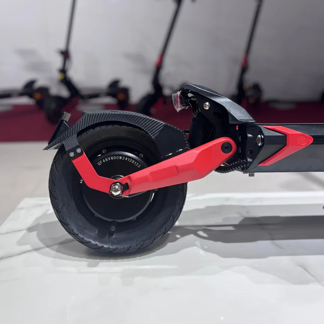 Izdelek je električni skiro, model Eco Speed 9. Na sliki je prikazana zadnja kolesna enota skiroja, ki vključuje robustno gumo in rdeče detajle na okvirju. V ozadju so vidni še drugi električni skiroji, kar nakazuje na okolje, kjer se izdelek prodaja. Skupaj daje vtis sodobnega in zmogljivega prevoznega sredstva.