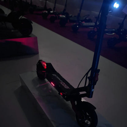 Na sliki je električni skiro model Eco Speed 9. Izdelek je črne barve in je postavljen na svetli podlagi, kar omogoča, da izstopajo detajli, kot so rdeče in modre luči. V ozadju so vidni tudi drugi električni skiroji, kar nakazuje, da gre za razstavo ali prodajno mesto. Scooter ima sodoben dizajn in je opremljen z LED lučmi, kar povečuje njegovo vidnost v temi.