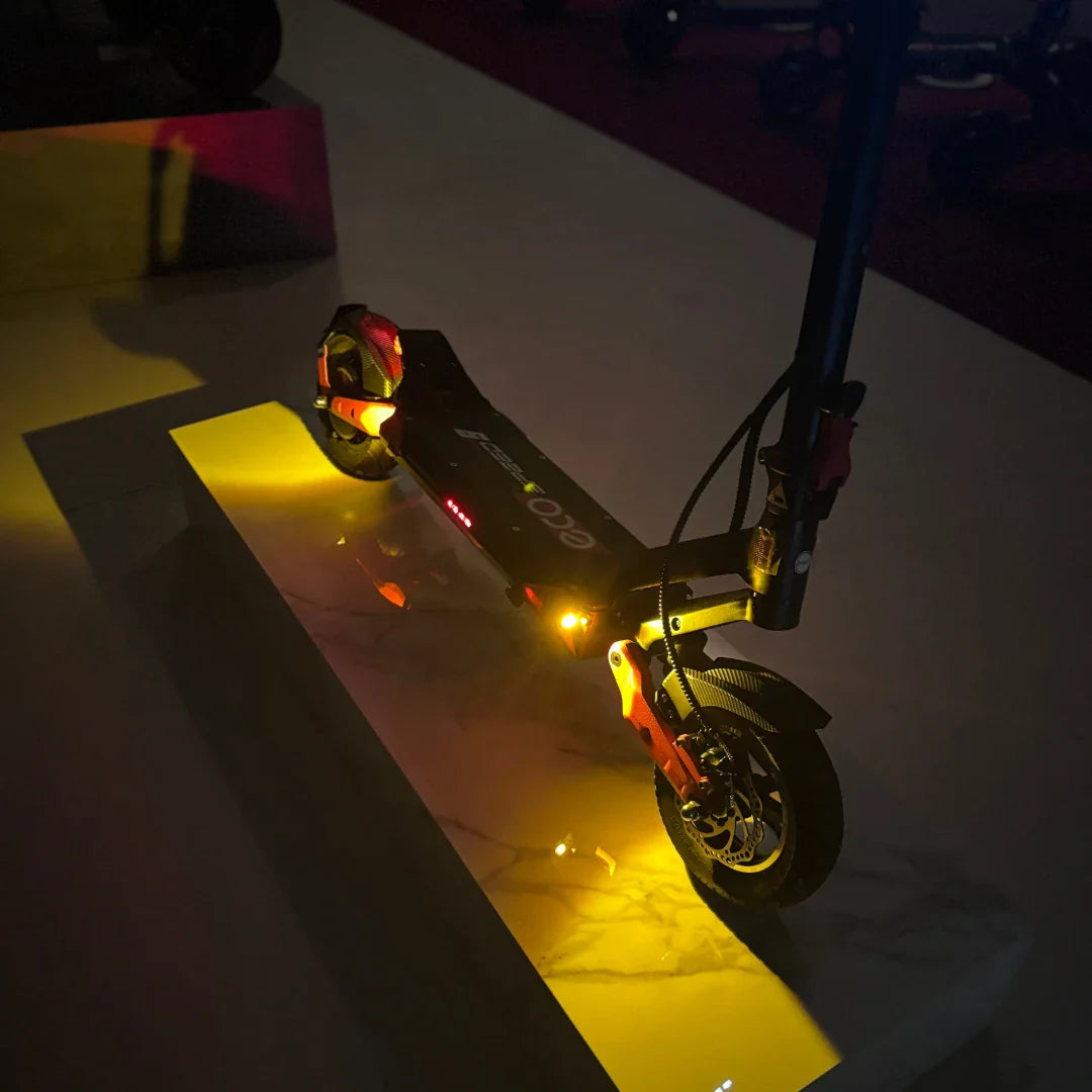 Na sliki je električni skiro model Eco Speed 9. Izdelek je postavljen na svetlečo podlago, kar poudarja njegovo obliko in detajle. Vidni so svetlobni elementi na skiroju, ki dodajajo dinamičen videz. Kolesa so opremljena z diskastimi zavorami, kar nakazuje na boljšo zmogljivost in varnost pri vožnji.