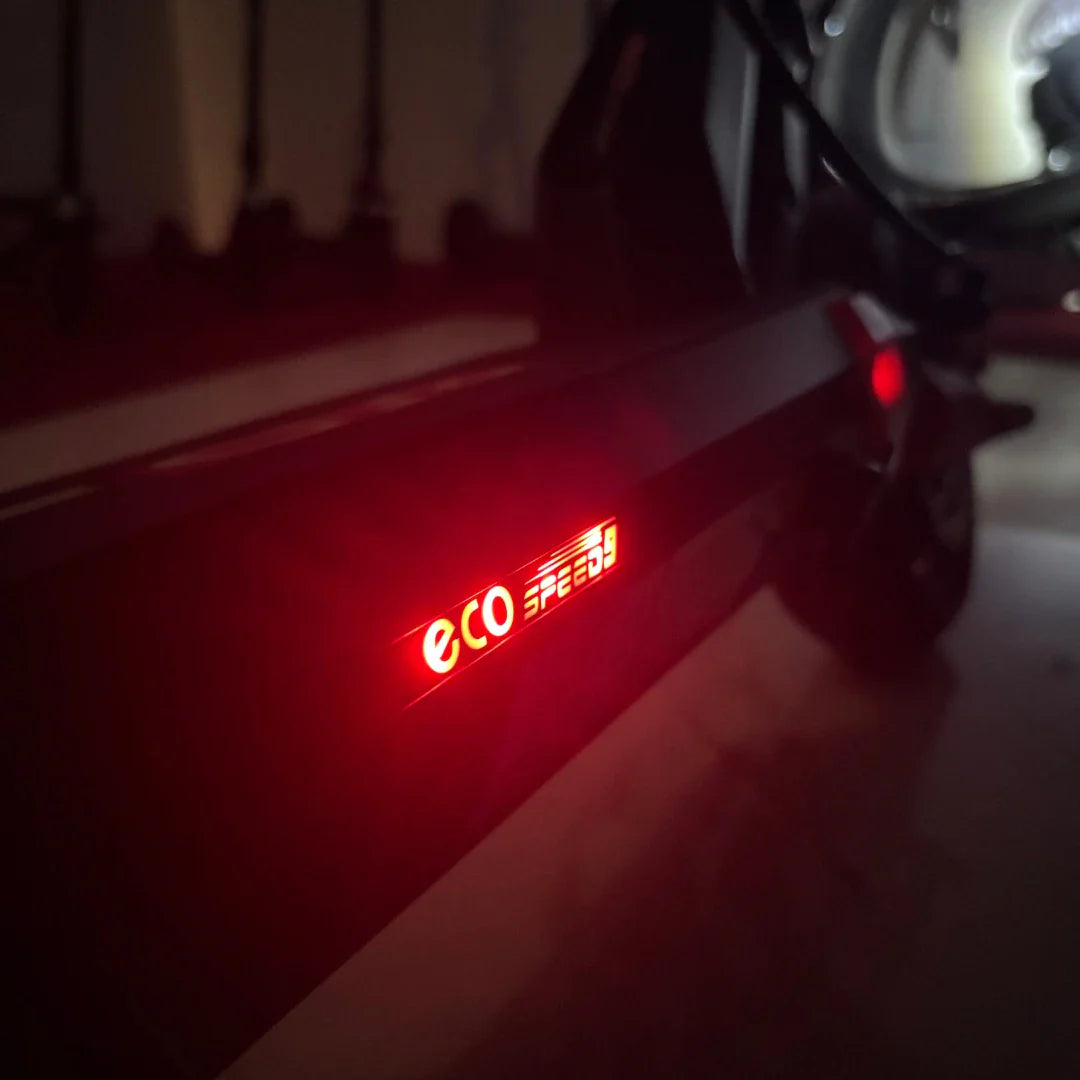 Na sliki je električni skiro model "Eco Speed 9". Vidna je osvetlitev z napisom "eco speed", ki nakazuje na način vožnje ali hitrost. Ozadje slike je temno, kar daje poudarek na svetlobnem elementu skiroja. Skuter je zasnovan za urbano mobilnost in udobno vožnjo.