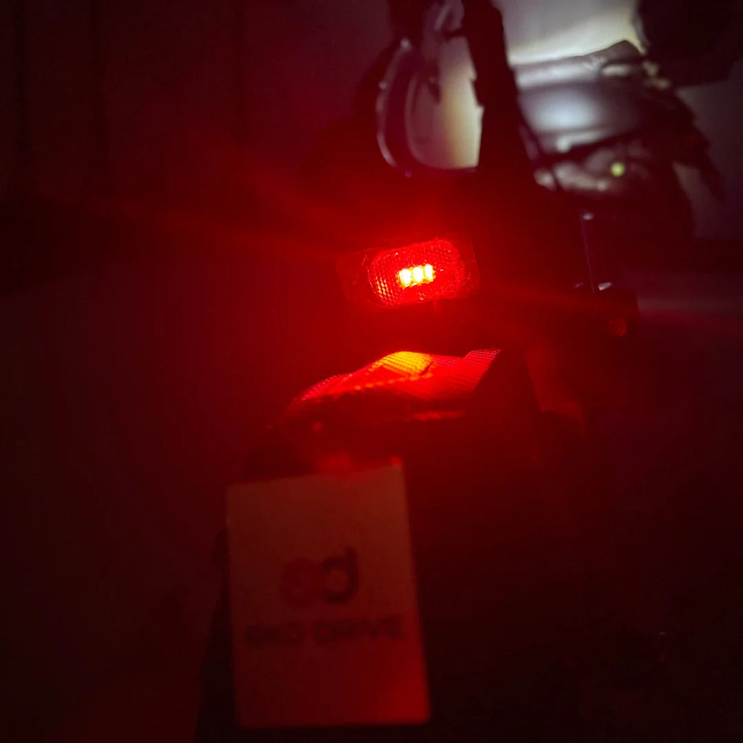 Na sliki je električni skiro model "Eco Speed 9". Vidna je zadnja lučka skiroja, ki sveti rdeče, kar nakazuje, da je skiro pripravljen za vožnjo. Prav tako je v ospredju oznaka znamke "SD" (Scoot Drive), ki je pritrjena na skiro. Ozadje je temno, kar dodatno poudarja svetlobo lučke.