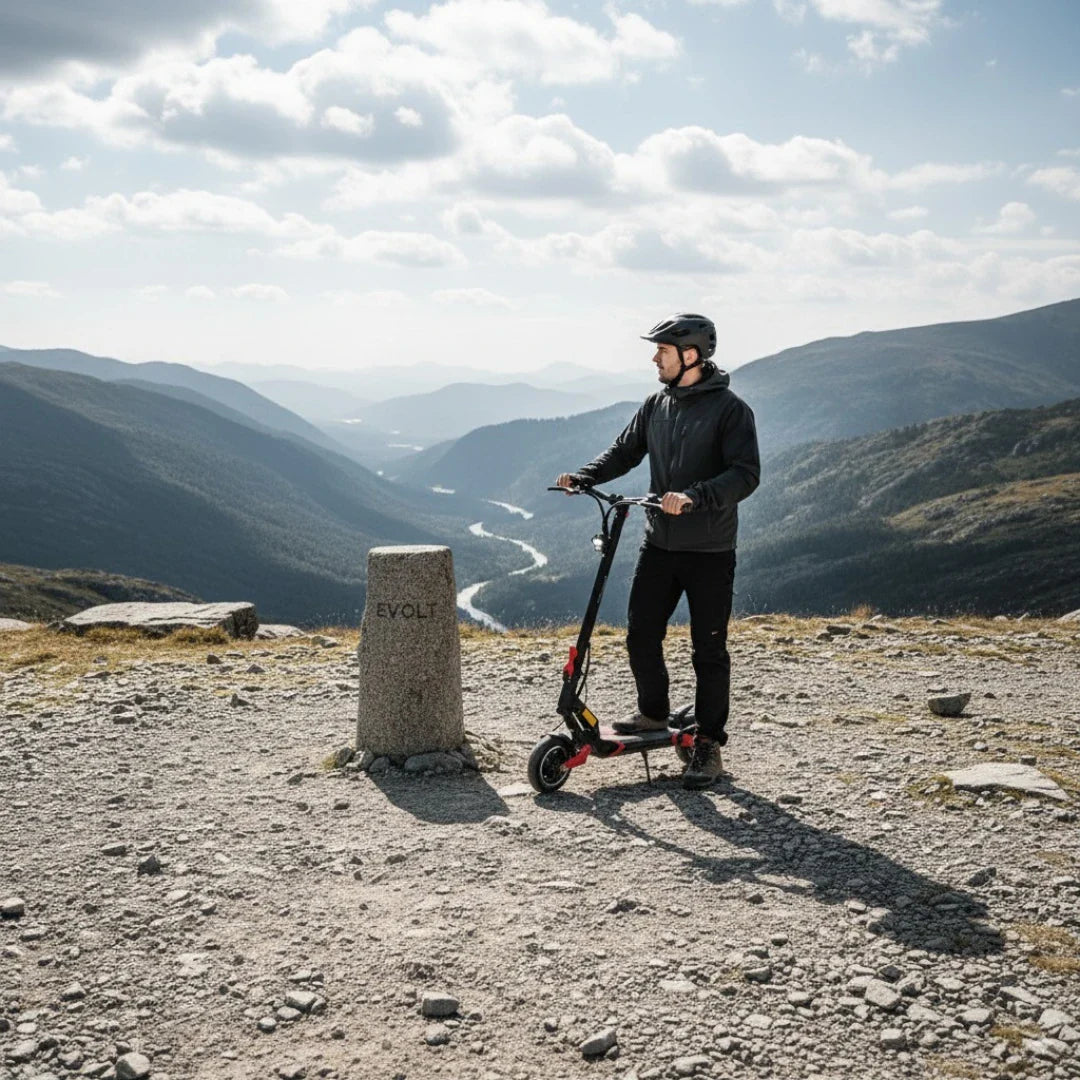 Na sliki je prikazan električni skiro model Eco Speed 9. Zasnova skiroja je moderna, s črnimi in rdečimi detajli. Oseba, ki ga uporablja, nosi čelado in športna oblačila, kar nakazuje, da je na prostem, verjetno na pohodniški poti. V ozadju se razprostira slikovita pokrajina z gorami in reko, kar dodaja občutek avanture in raziskovanja.