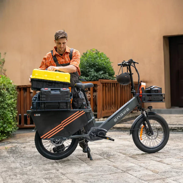 Na sliki je električno kolo znamke Engwe, model LE20. Kolo je opremljeno z različnimi škatlami za shranjevanje, kar nakazuje na njegovo praktično uporabo. Oseba na sliki se ukvarja z organizacijo opreme, kar kaže na uporabnost kolesa za prevoz orodja ali drugih predmetov. Kolo ima robustno zasnovo in je primerno za mestno vožnjo ali dostavo.