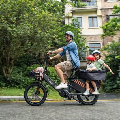 Na sliki je električno kolo znamke Engwe, model LE20. Prikazuje moškega, ki vozi kolo po cesti, medtem ko sta na zadnjem delu kolesa dva otroka v posebnem sedežu. V ozadju so drevesa in stavbe, kar ustvarja prijetno urbano okolje. Moški nosi čelado in se nasmehne, kar nakazuje na užitek pri vožnji.