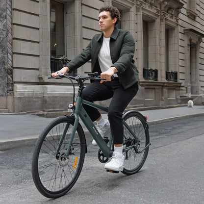 Izdelek je električno kolo znamke Engwe, model Mapfour N1 Air. Na sliki je moški, ki se vozi na tem kolesu po mestni ulici. Kolo ima moderno zasnovo, z značilnimi širokimi pnevmatikami in elegantnim okvirjem v temno zeleni barvi. Moški nosi športno obleko, kar nakazuje na sproščeno vožnjo v urbanem okolju. V ozadju so vidne mestne zgradbe, kar dodatno poudarja mestno atmosfero.