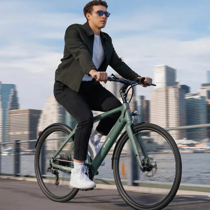 Na sliki je električno kolo znamke Engwe, model Mapfour N1 Air. Prikazuje moškega, ki vozi kolo po mestni promenadi, obdanem z modernimi zgradbami. Kolo ima minimalističen dizajn v zeleni barvi, moški pa nosi sončna očala in športna oblačila.