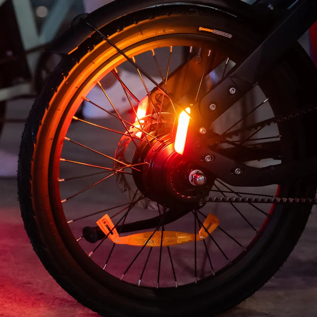 Na sliki je električno kolo, model Engwe P20. Vidna je zadnja pnevmatika s kolesnim motorjem in svetlobnimi elementi, ki zagotavljajo vidnost. Kolo ima tudi odsevnike na pedalih, kar povečuje varnost pri vožnji v temi.