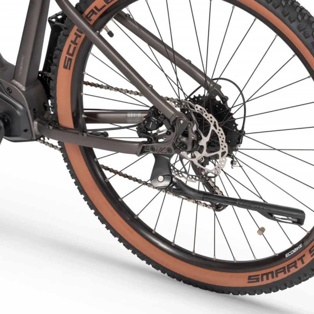 Izdelek je električno kolo, model Ecobike SX300. Na sliki je prikazan del kolesa, vključno s pogonom, zadnjim kolesom in zavorami. Kolo ima široke pnevmatike z rjavim robom ter disk zavore, kar nakazuje na primernost za vožnjo po različnih terenih. Vidna je tudi oznaka znamke Ecobike na pnevmatikah.