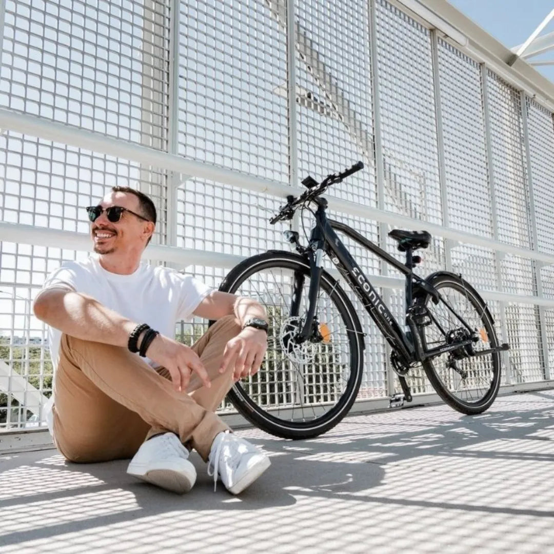 Moški sedi ob električnem kolesu Econic One Smart Urban na modernem mostu.