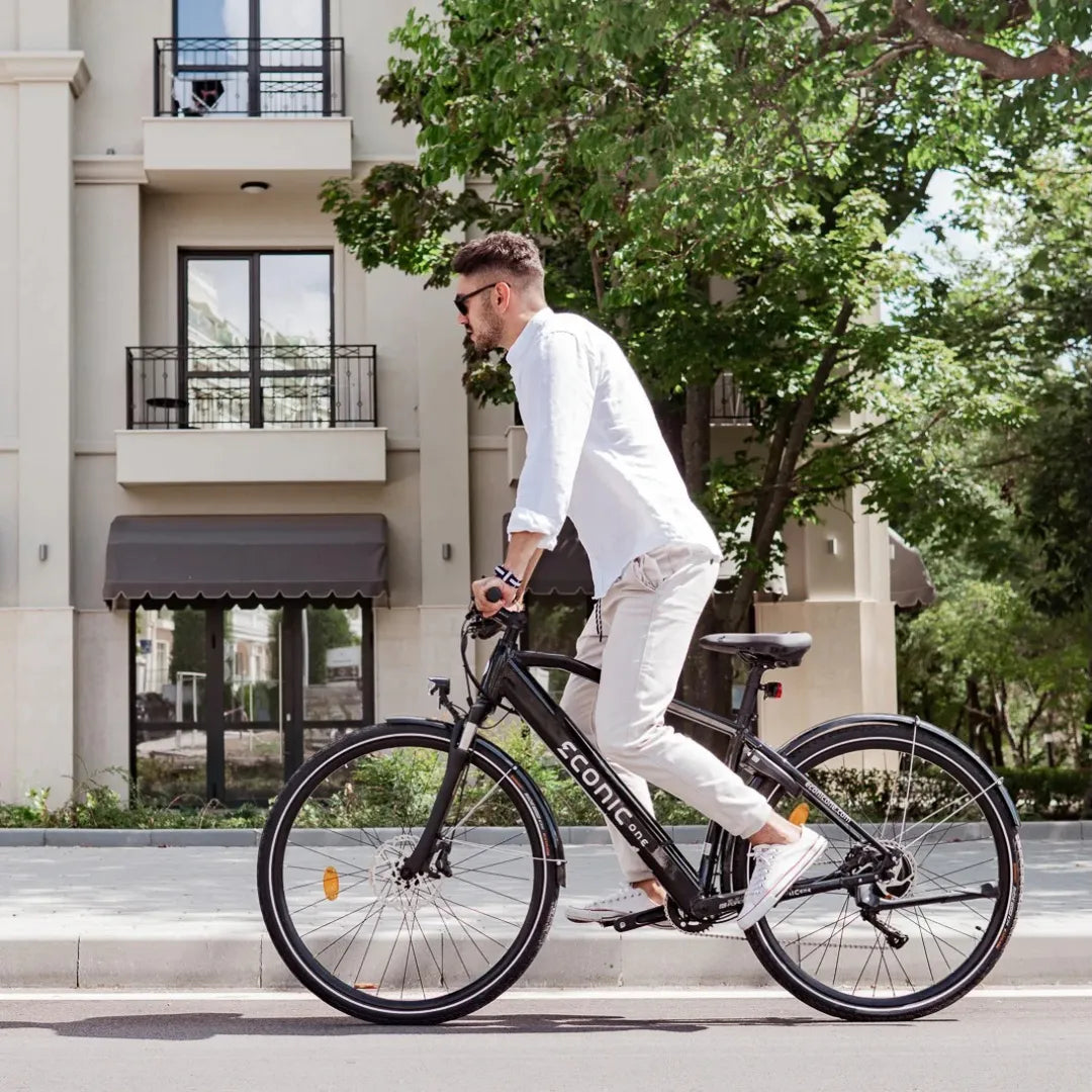 Moški se vozi z električnim kolesom Econic One Smart Urban po mestni ulici blizu modernih zgradb.