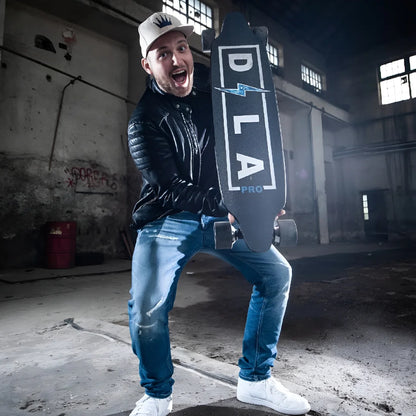 Oseba v usnjeni jakni drži električni skejtbord Dila Pro in se smeji v industrijskem prostoru.