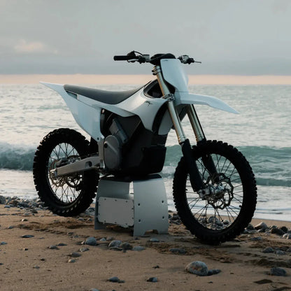 Električni motokros motocikel Stark Varg parkiran na plaži z valovi v ozadju.