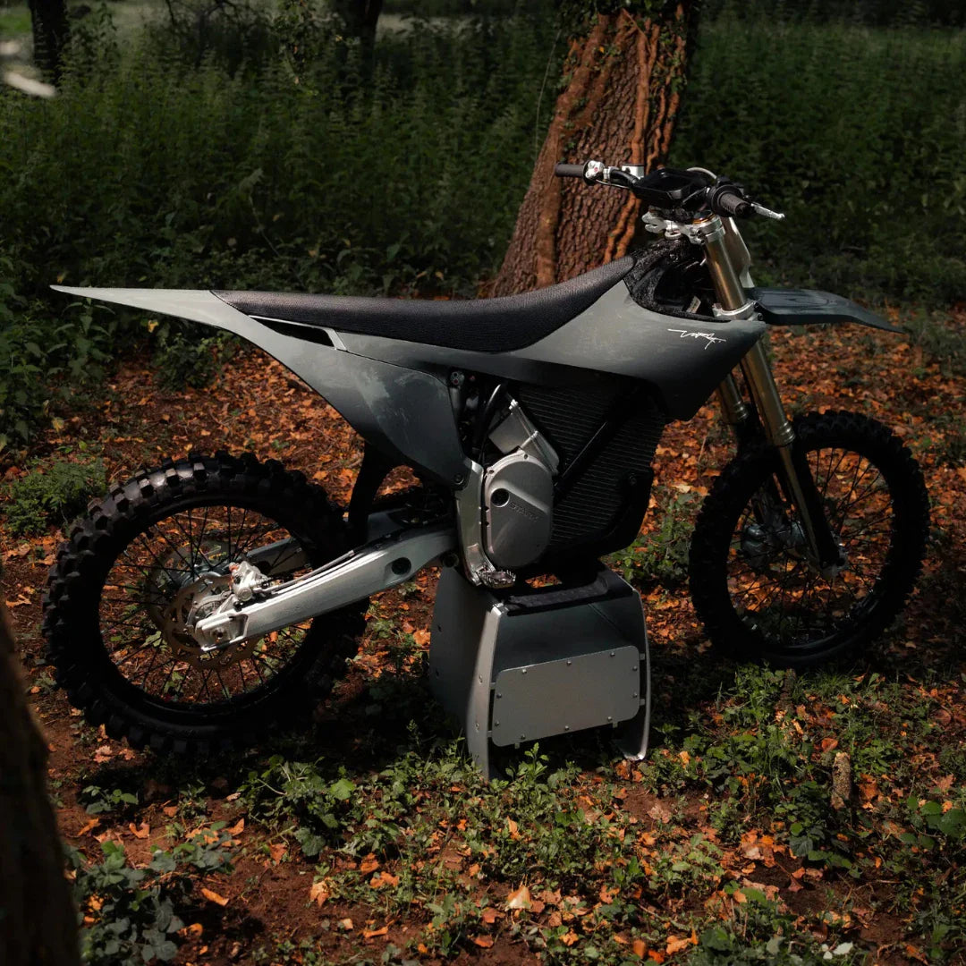 Električni motokros Stark Varg parkiran med drevesi in listjem na gozdnatem območju.