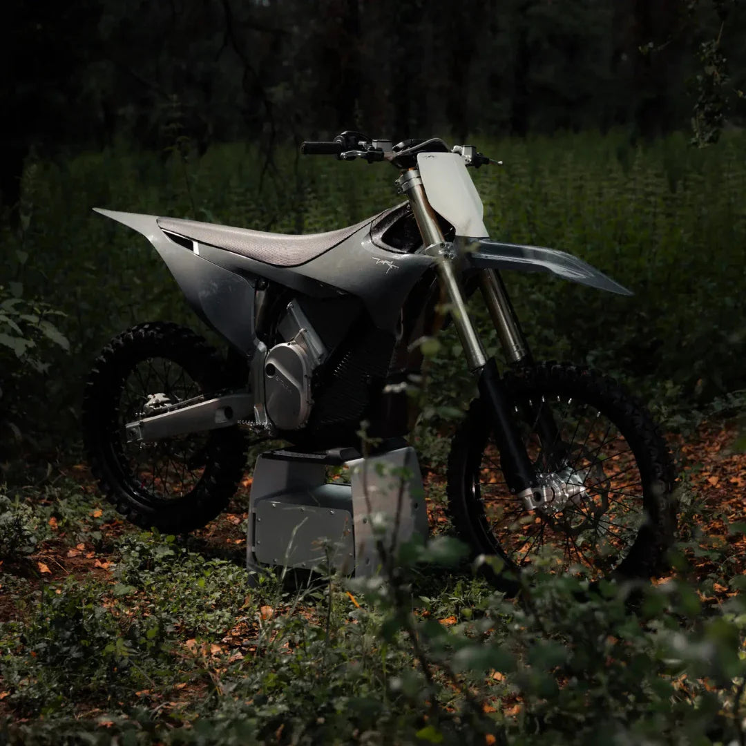 Električni motokros Stark Varg v gozdnem okolju, obdan z zelenjem in odpadlim listjem.