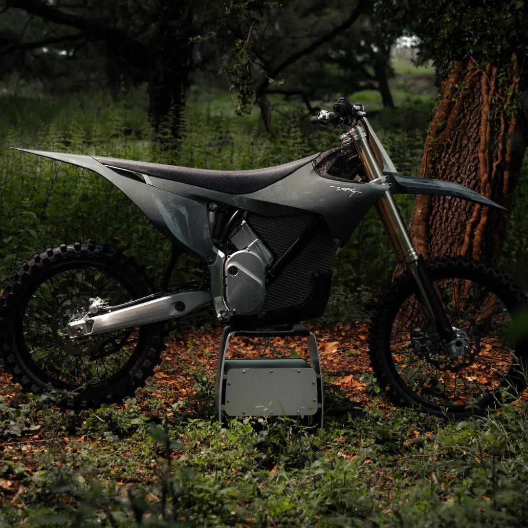 Električni motokros motocikel Stark Varg parkiran v bujnem, zelenem gozdnem okolju.