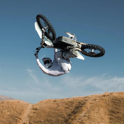 Jezdec izvaja trik na električnem motokros kolesu Stark Varg s čisto nebo v ozadju.