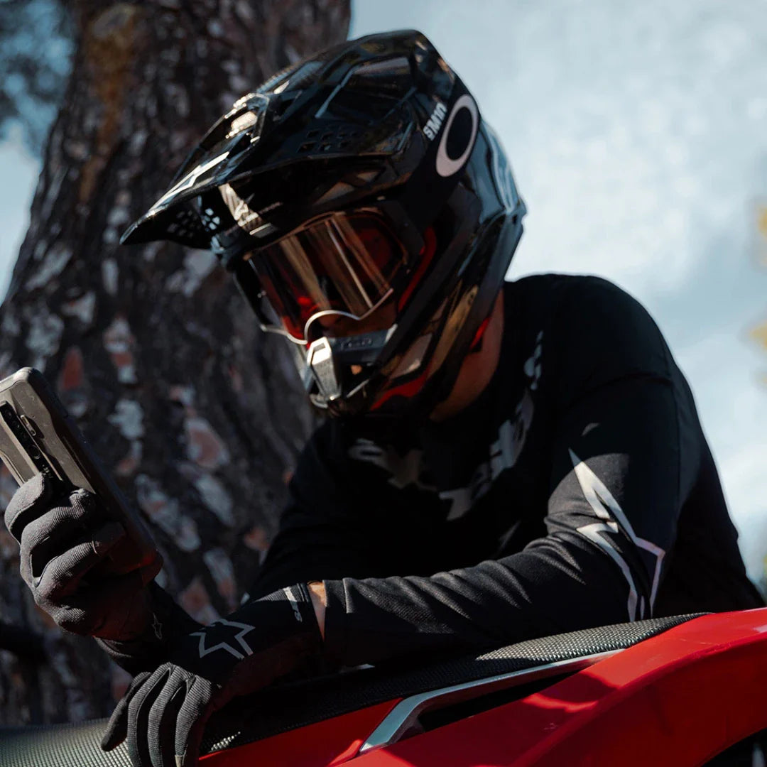 Voznik s črno čelado preverja svoj telefon ob električnem motokros kolesu Stark Varg.