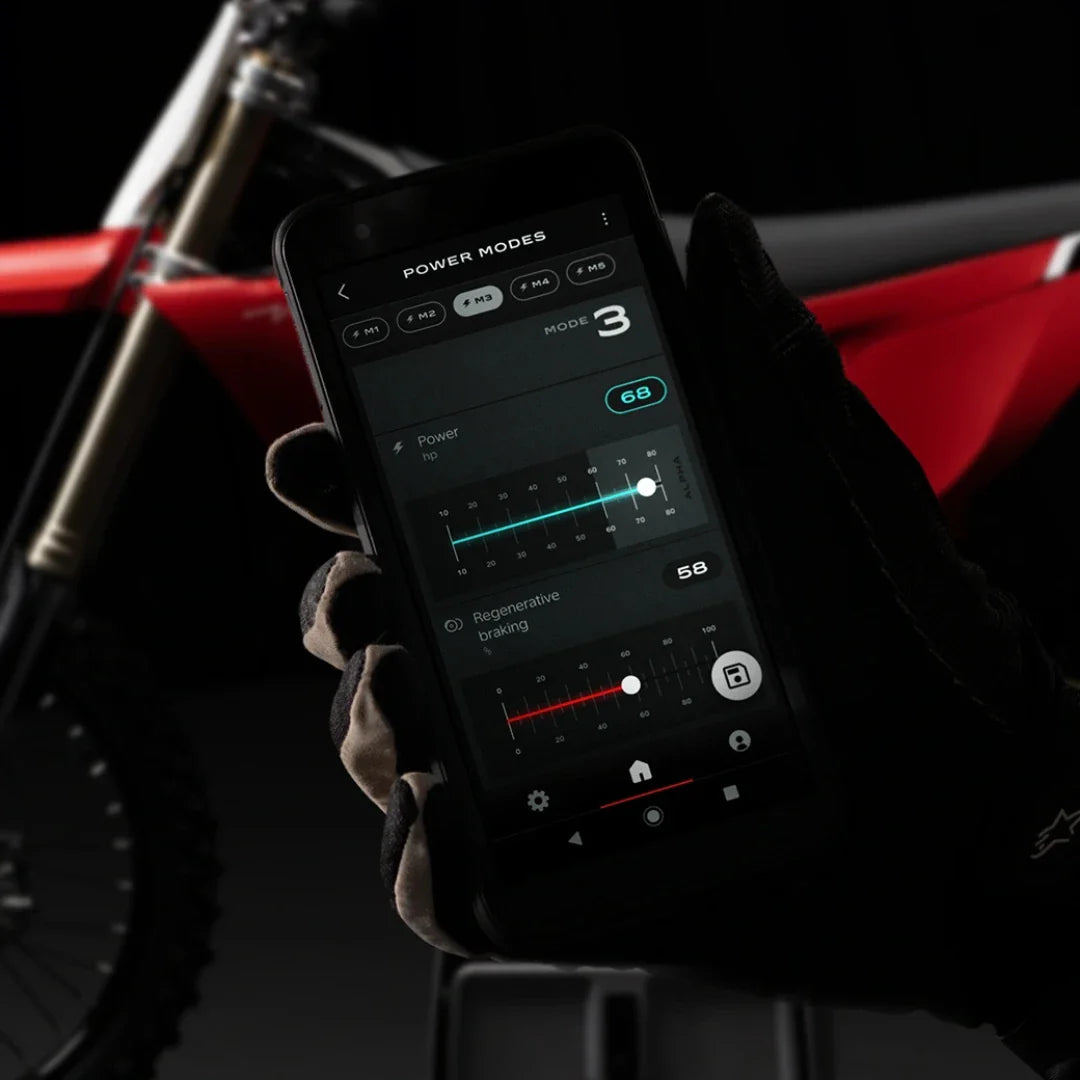 Roka v rokavici drži pametni telefon, na katerem so prikazane nastavitve za električni motokros motocikel Stark Varg.