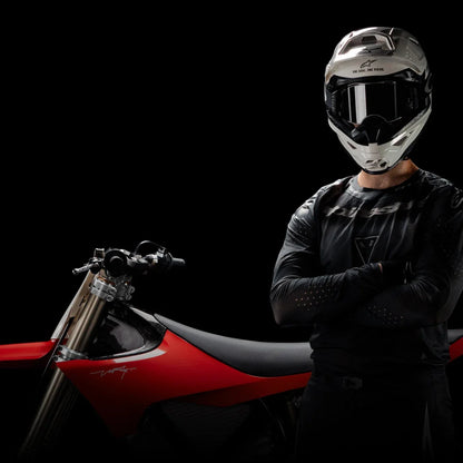 Voznik s čelado stoji samozavestno ob električnem motokros kolesu Stark Varg.