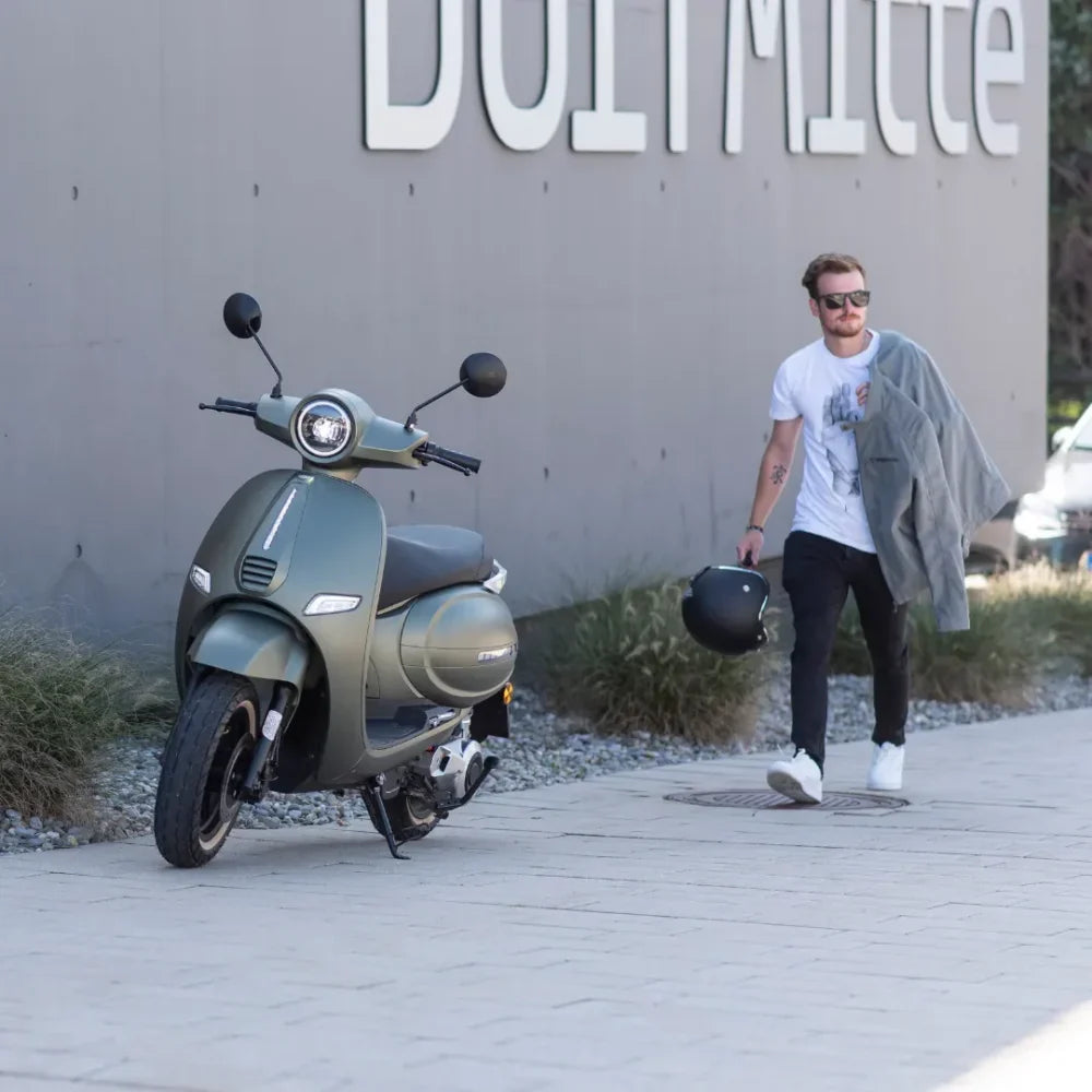 Moški hodi ob električnem skuterju Efo Et3000, parkiranem na pločniku.