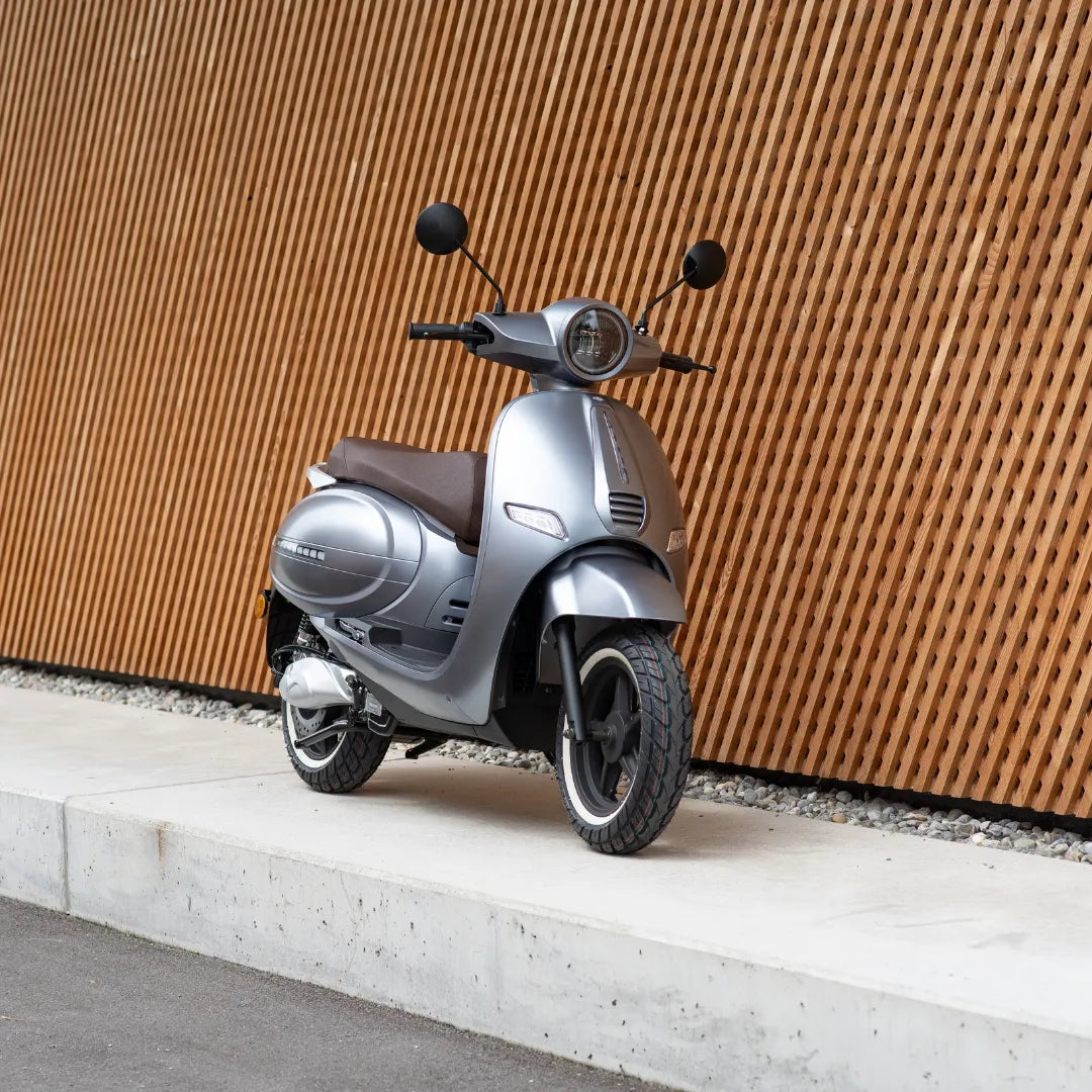 Električni skuter Efo Et3000 parkiran ob leseni steni, odlikuje ga eleganten srebrn dizajn.