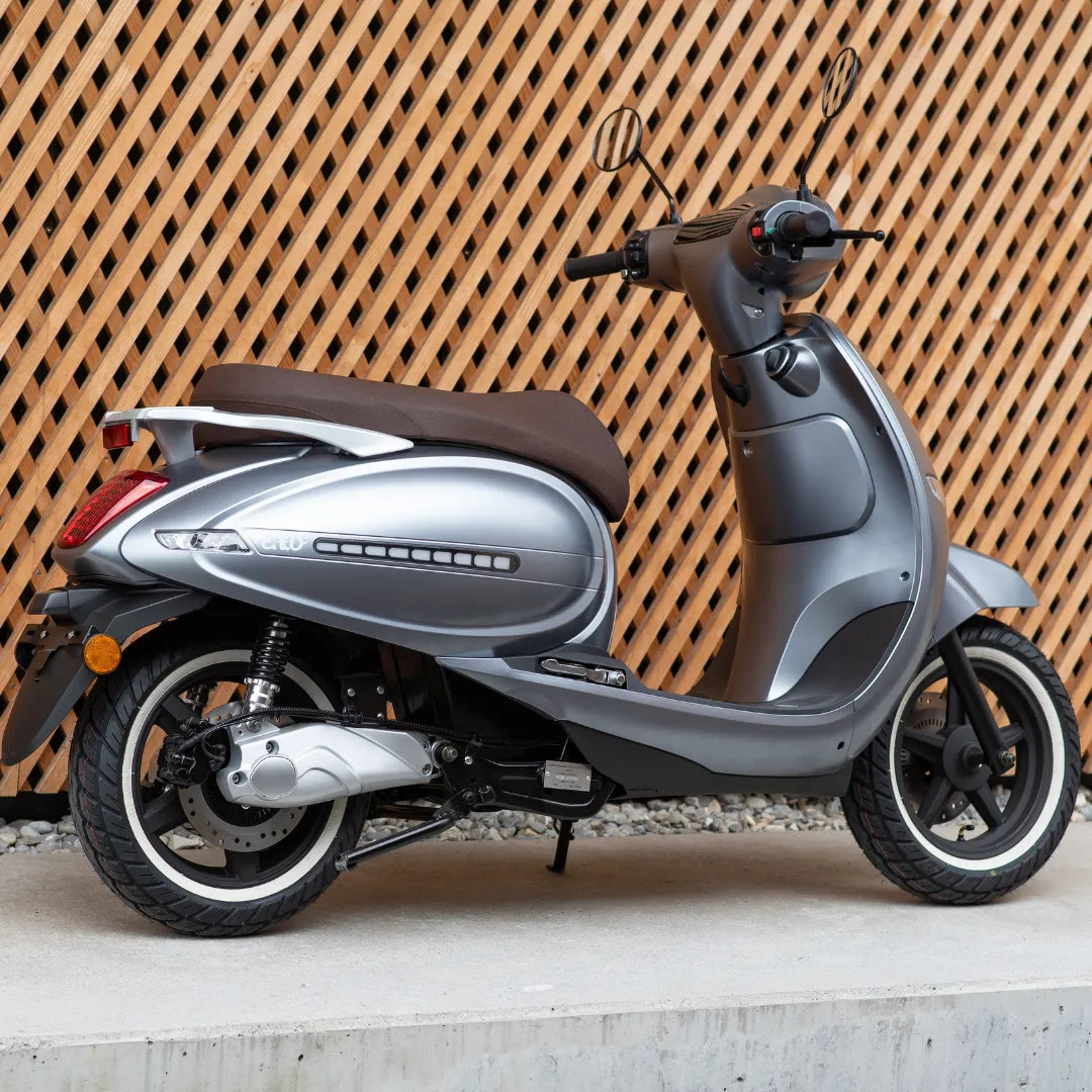 Električni skuter Efo Et3000 v srebrni barvi, parkiran ob ozadju z leseno mrežo.