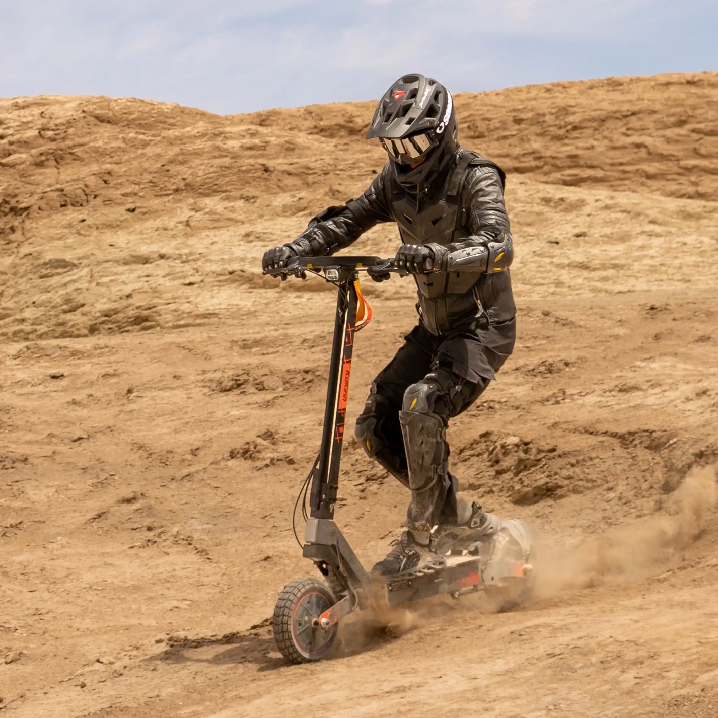 The product in the picture is an electric scooter, model Kukirin G2 Ultra. A person wearing protective gear is seen riding the scooter on uneven terrain. Dust is rising around them, indicating a dynamic ride.