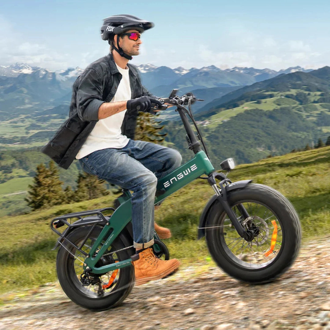 Izdelek na sliki je električno kolo, znamke Engwe, model EP-2 3.0 Boost. Na sliki je videti moškega, ki vozi to električno kolo po naravnem okolju, obdanem z gorami in zelenjem. Kolo ima široke gume, kar je značilno za terenska kolesa, in moški nosi čelado ter zaščitne rokavice.